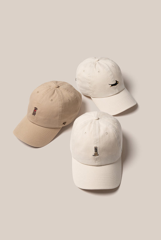 Slide 1:Three beige '47 hats with dog icons on the front, in a flat lay image