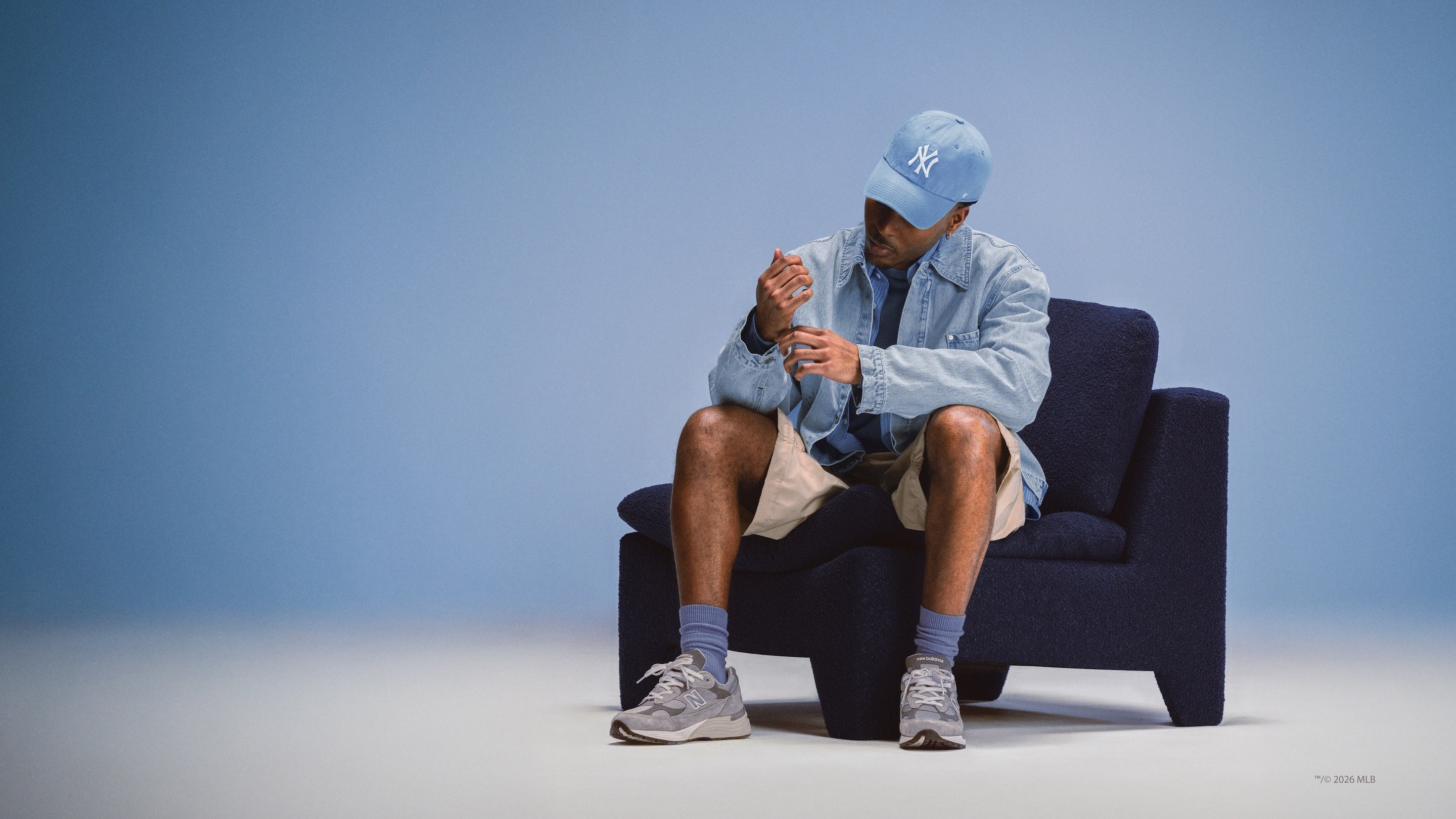 Person wearing a light blue cap and jacket sitting on a dark blue chair against a light blue background