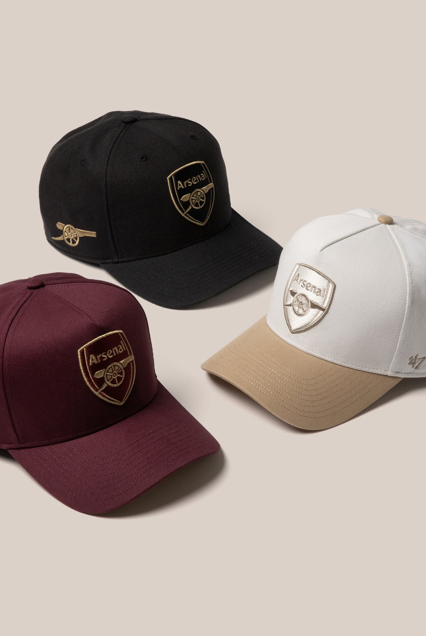 A product image of three Arsenal hats. Maroon and Black with gold Arsenal logos and a white and brown hat with silver logos