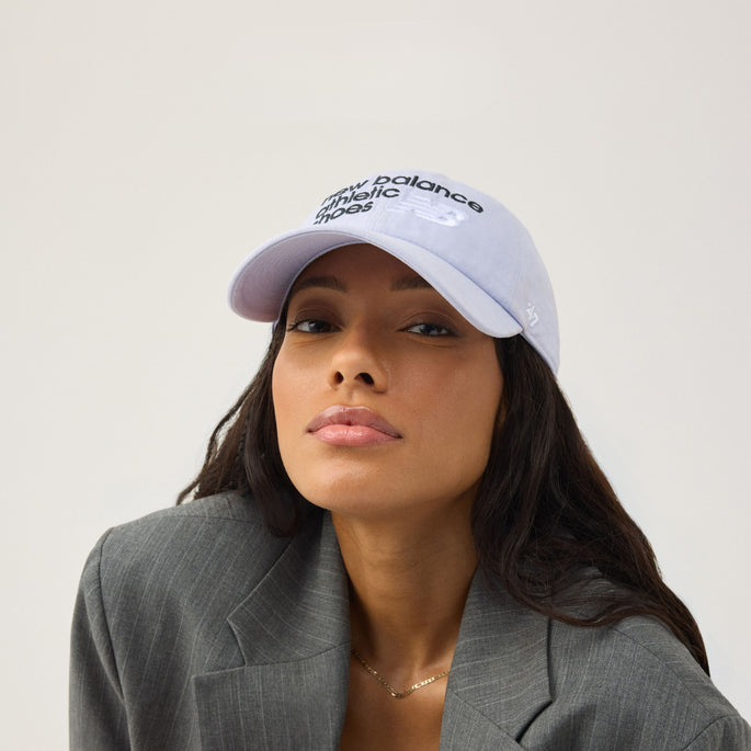 A women with long dark hair wearing a grey blazer and a light purple New Balance by '47 cap