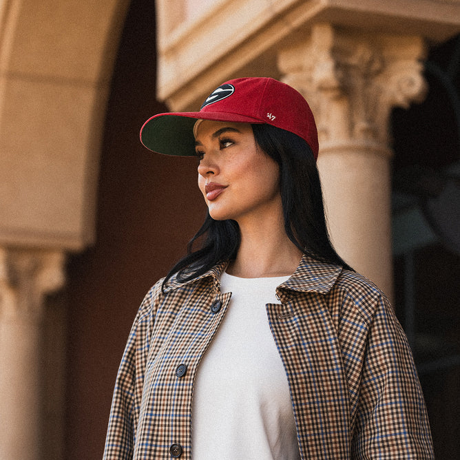 Woman wearing a New York Giants '47 red cap and checkered jacket standing in front of a building.