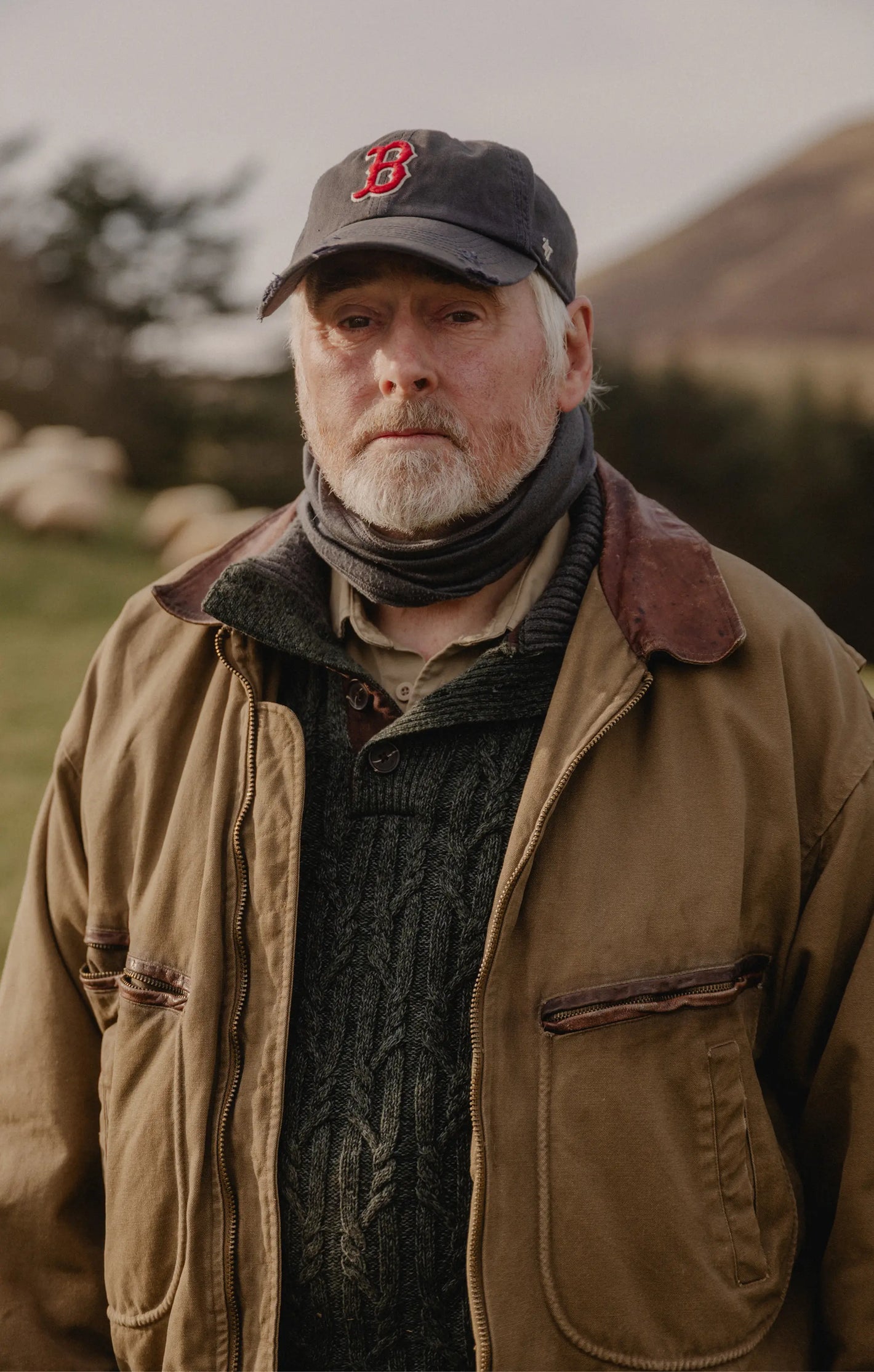 A picture of an older man in a barn jacket wearing a navy '47 Boston Red Sox hat with mountains in the background 